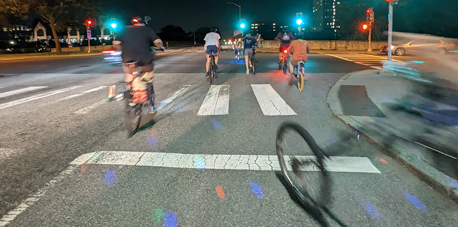 a group of bicycle choppers embark at a green light at a city intersection at night