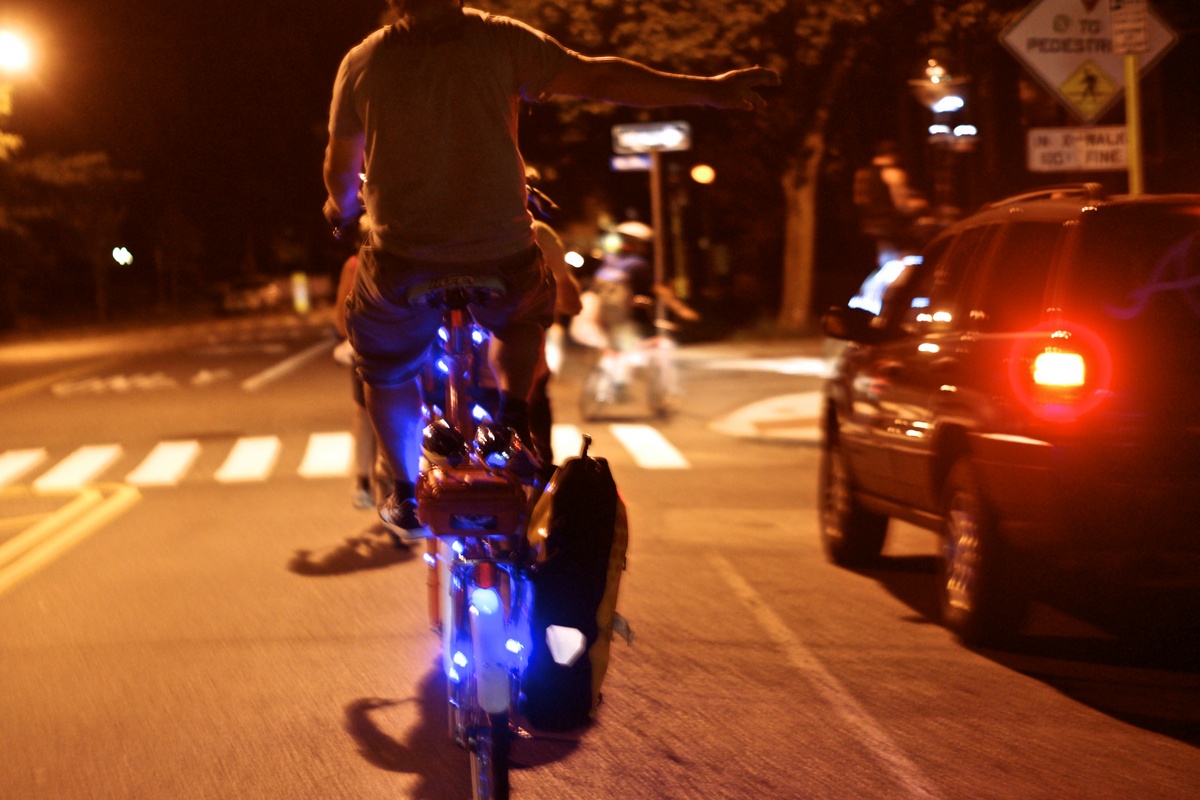 a cyclist riding a brightly lit tallbike signals a right-hand turn