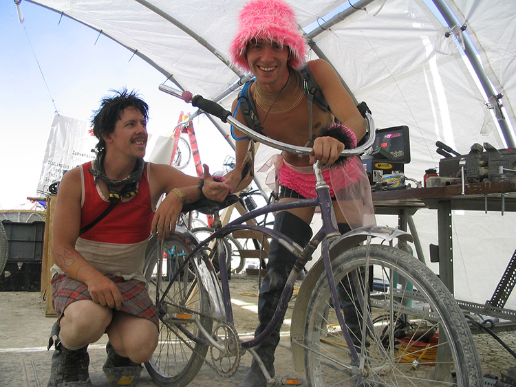 two proud bicycle frame repairers pose with their rewelded bicyle in Kwanza hut at Burning Man